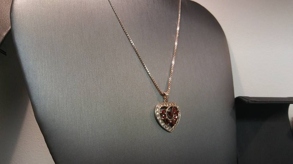 Gold necklace with a heart-shaped pendant on a black display.