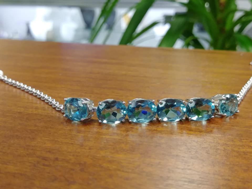 Silver necklace with six blue oval gemstones on a wood surface, greenery in background.