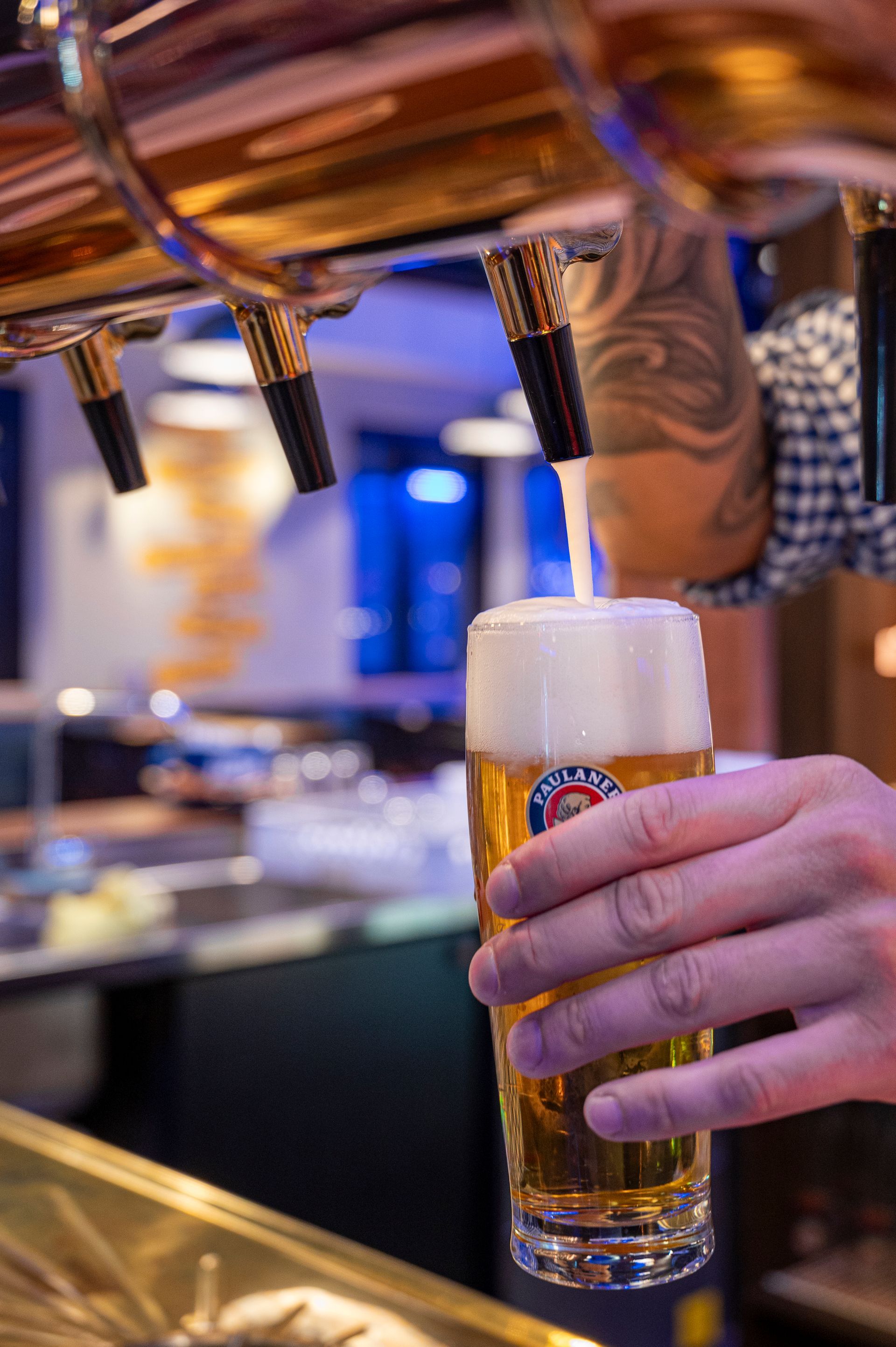 Mano che regge un bicchiere di birra sullo sfondo sfocato delle luci della città di notte.