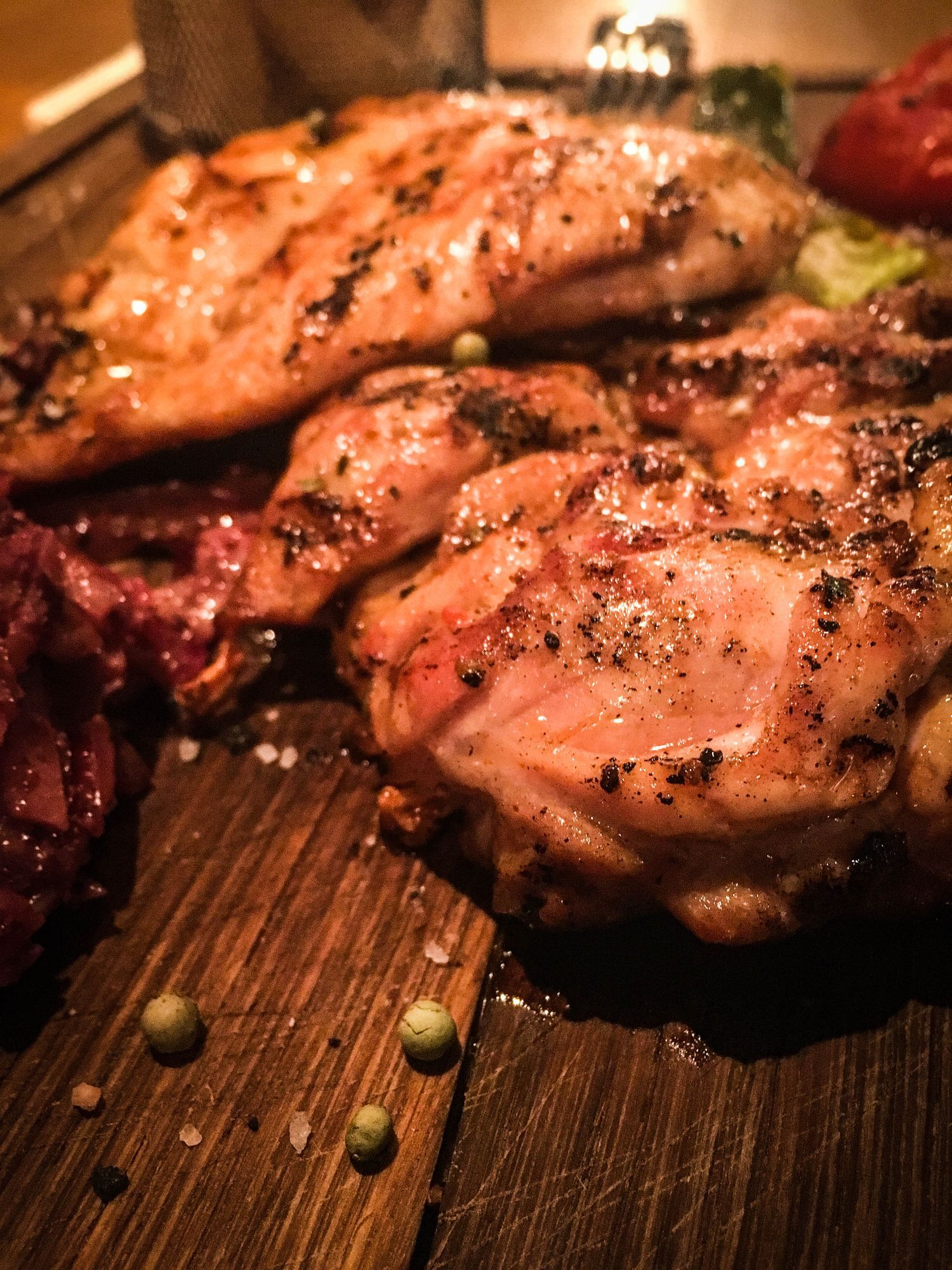 Pollo alla griglia su un tagliere di legno con verdure e condimenti; luce calda.