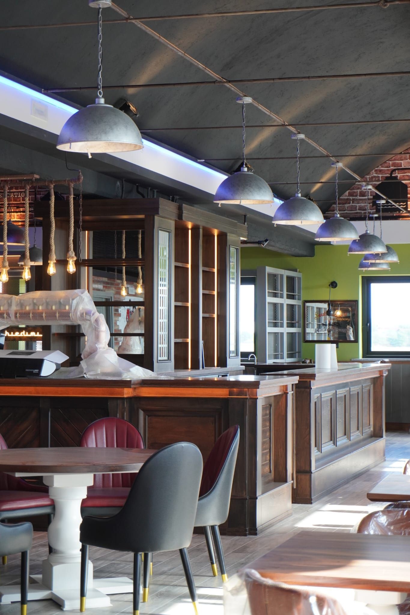 Ristorante interno con bancone e tavoli in legno, lampade a sospensione e sedie color bordeaux e nero.