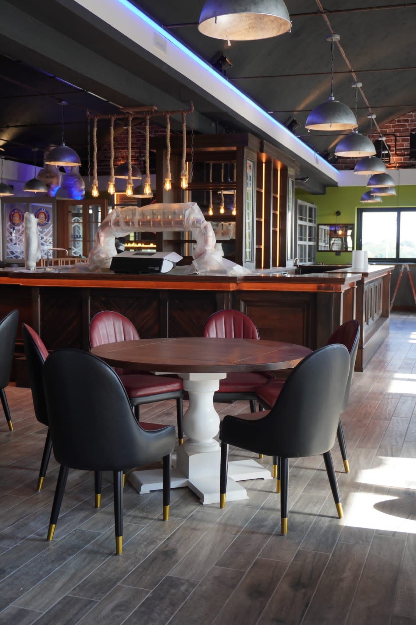 Zona pranzo con tavolo rotondo in legno, sedie nere e un bar sullo sfondo.