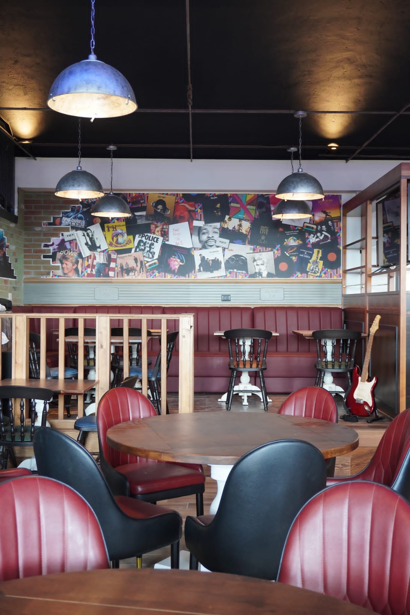 Vista interna di un ristorante con tavoli e sedie. Sedie in pelle rossa e nera circondano un tavolo in legno; parete decorata con mattoni a vista.