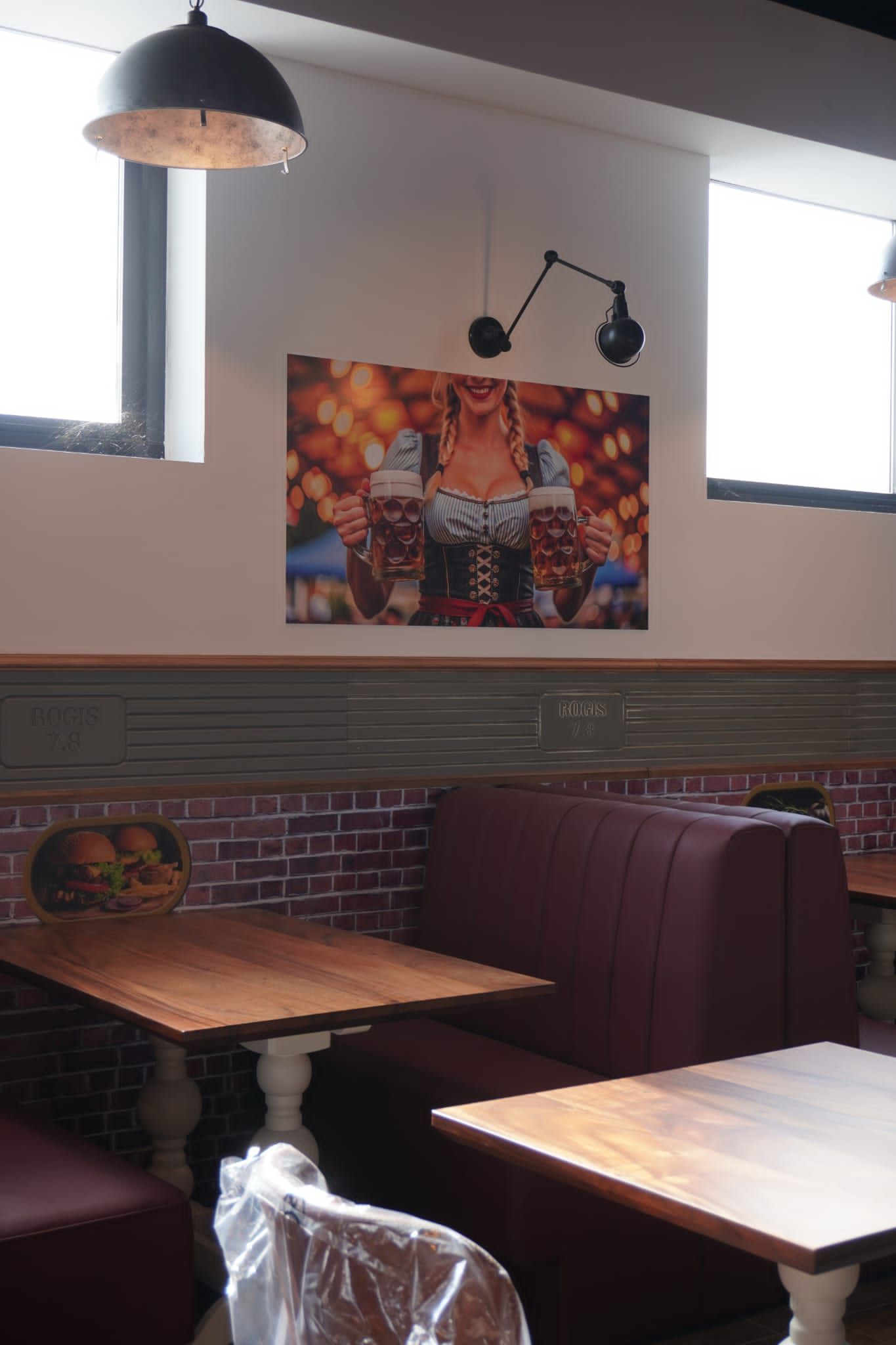 Interno di un ristorante con cabine, tavoli, muro di mattoni e un quadro a tema Oktoberfest.