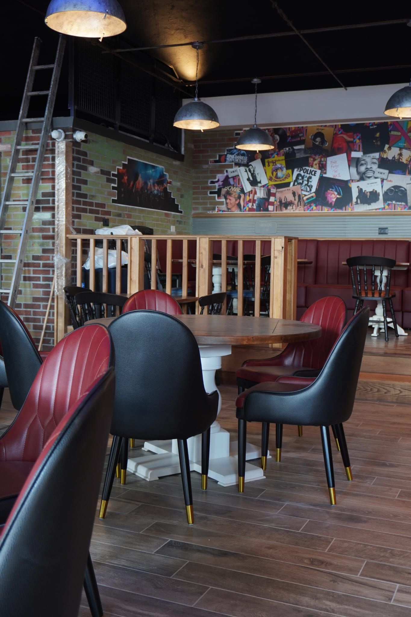Interno di un ristorante con tavolo rotondo, sedie rosse e nere, pareti ricoperte di mattoni e dischi e una scala.