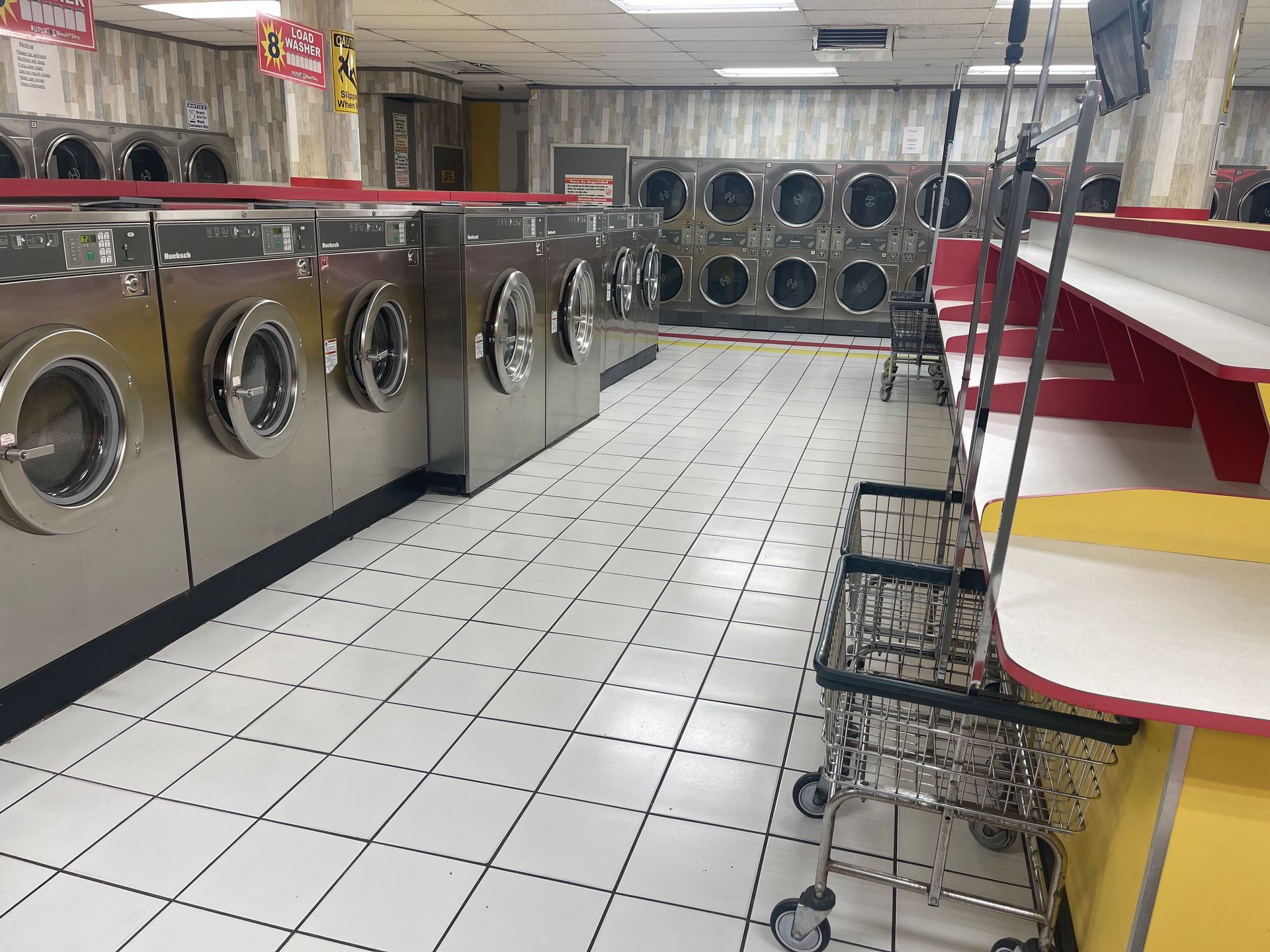 Interior of a laundromat with rows of washing machines, a folding table, and empty laundry carts.