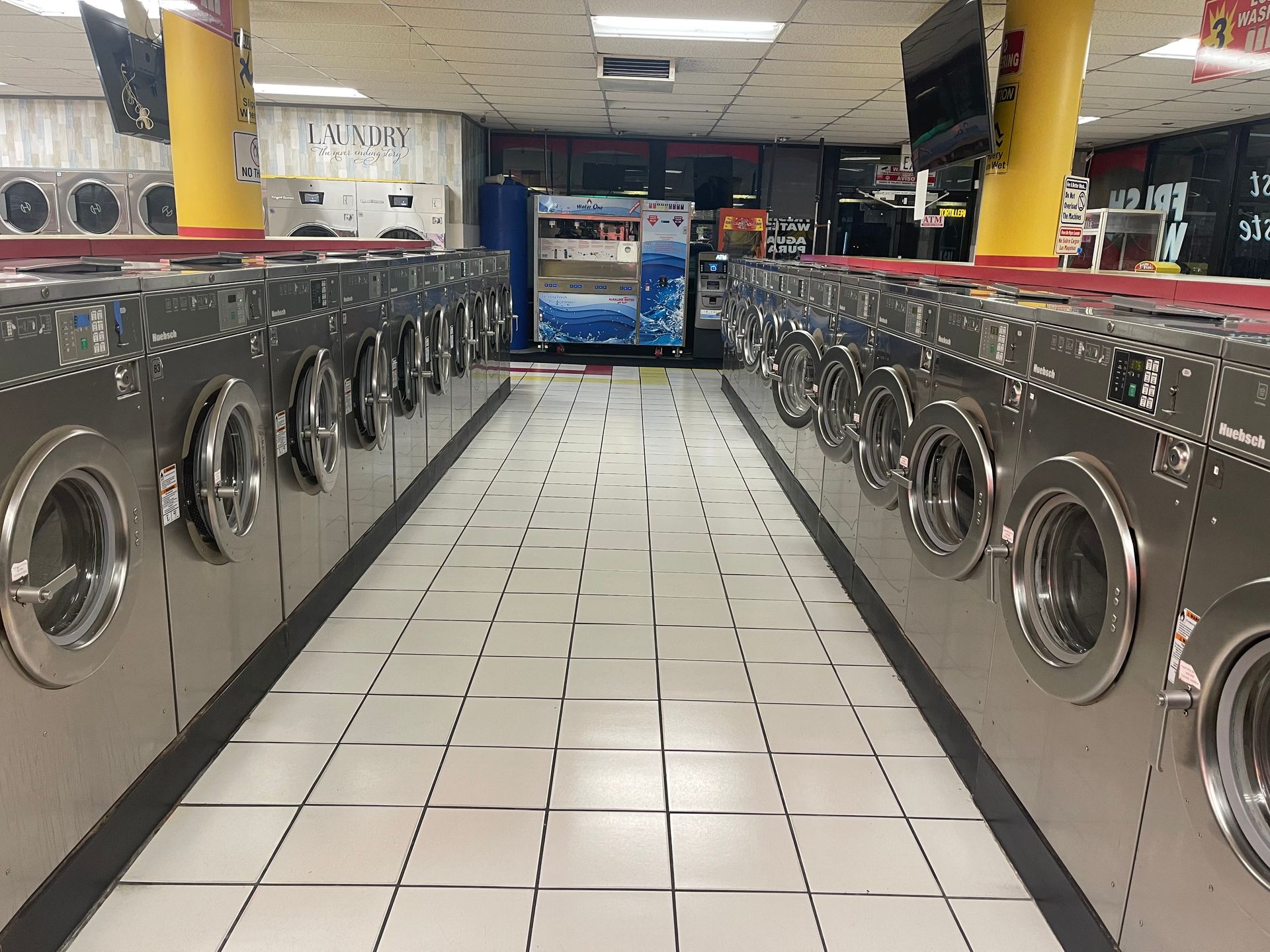 A laundromat with rows of silver washing machines and a white tiled floor.