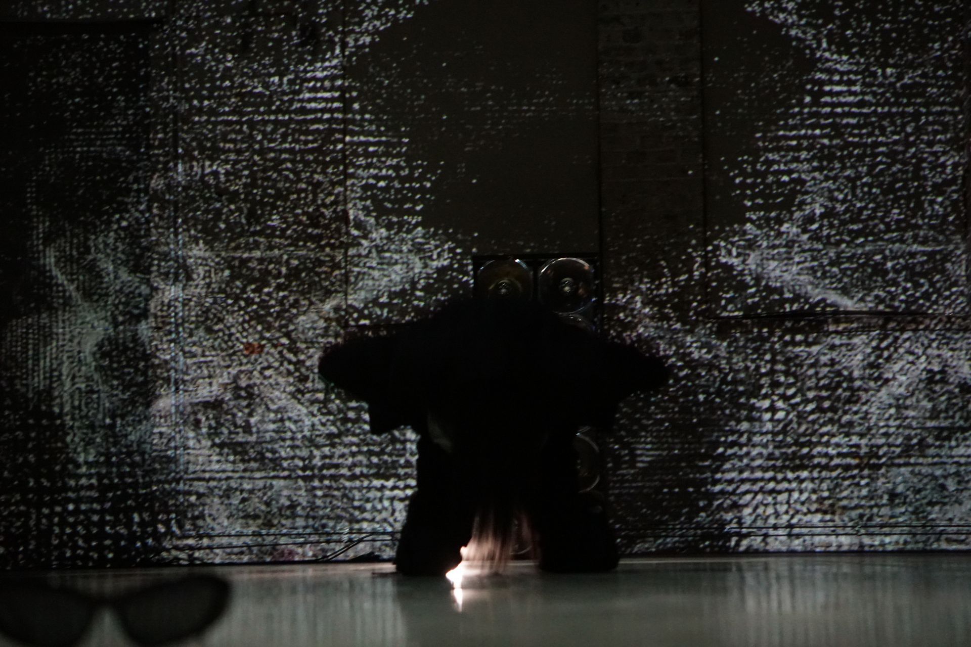 A dancer performs a center split on a dark, dimly lit stage, illuminated by a pool of cool blue light.