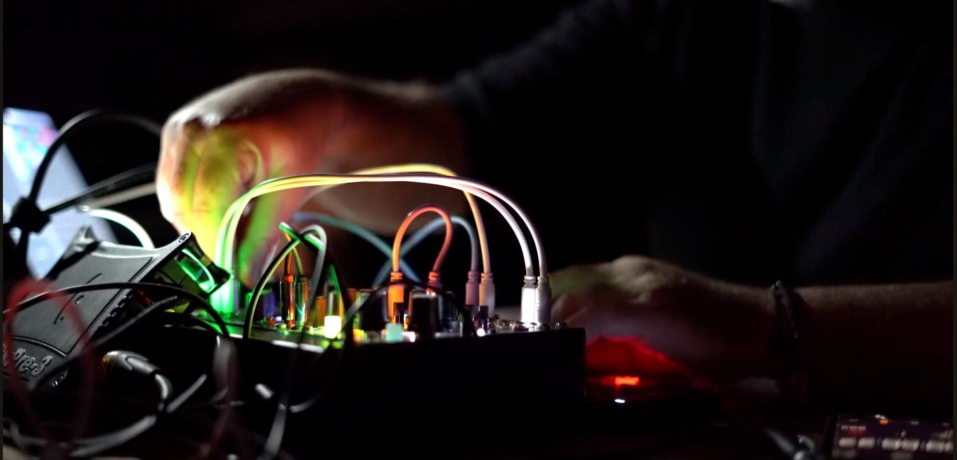 A person adjusts colorful glowing patch cables on a modular synthesizer in a dimly lit setting.