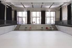A spacious, white-floored studio with tiered seating platforms, large windows, and dark curtains against the walls.