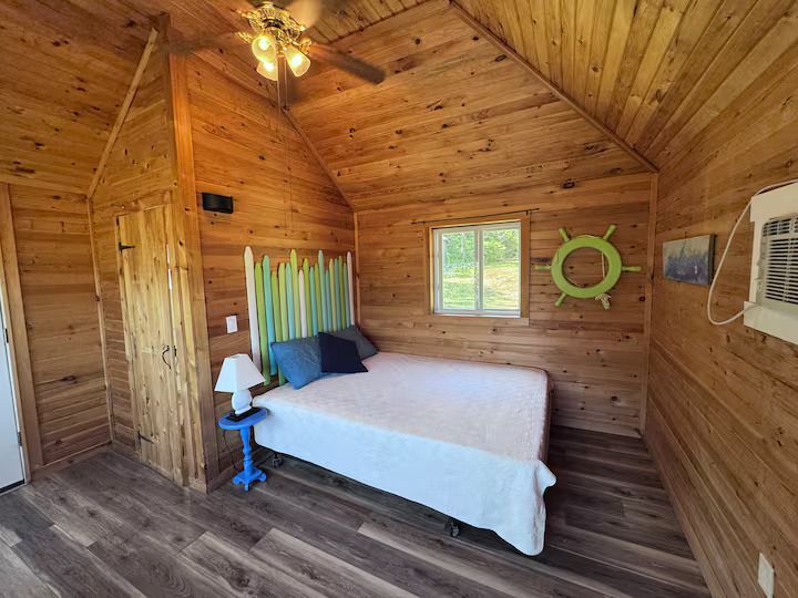 Wooden cabin bedroom with a bed, colorful headboard, window, wall mirror, and air conditioner