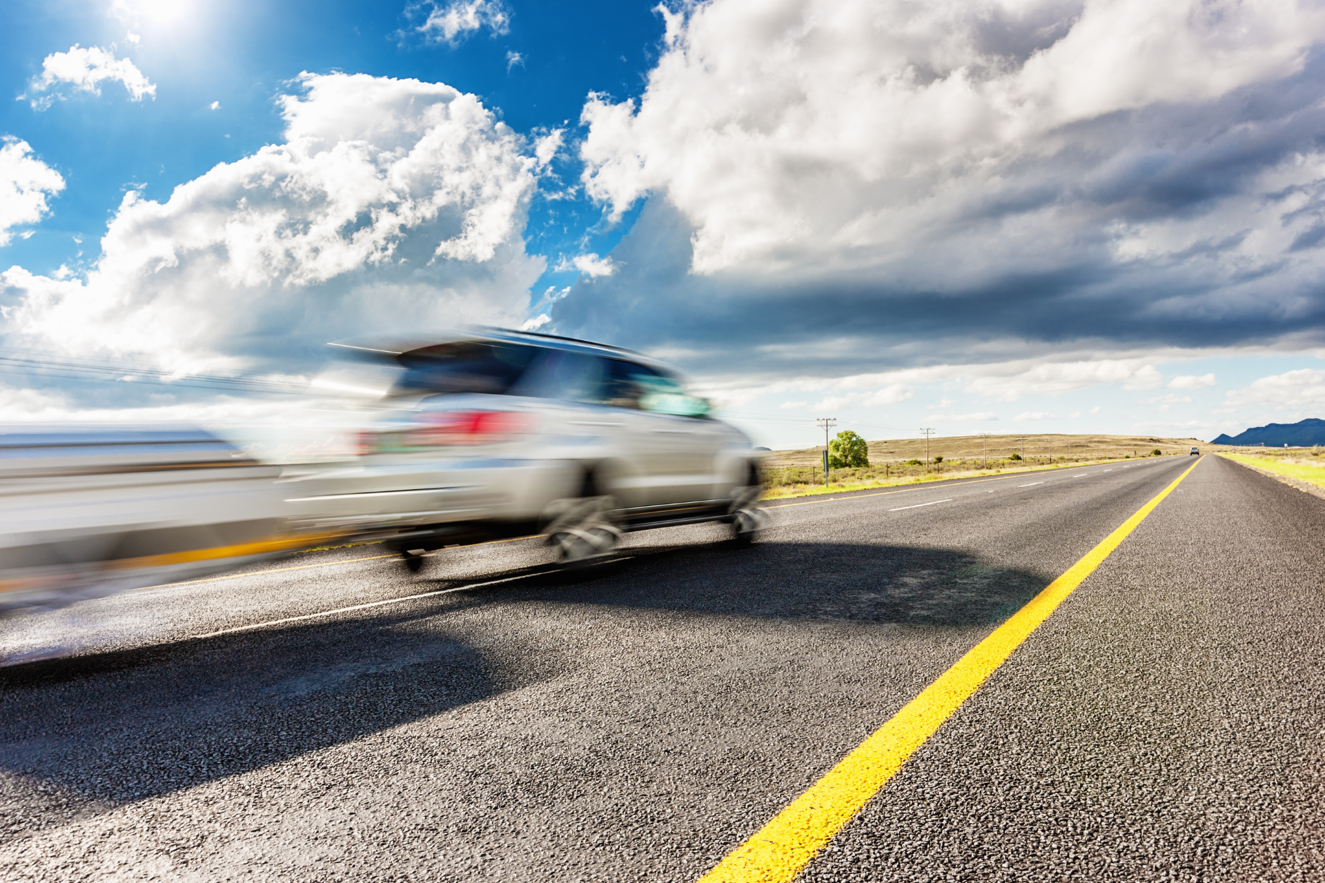 A car is driving down a highway with a cloudy sky in the background.