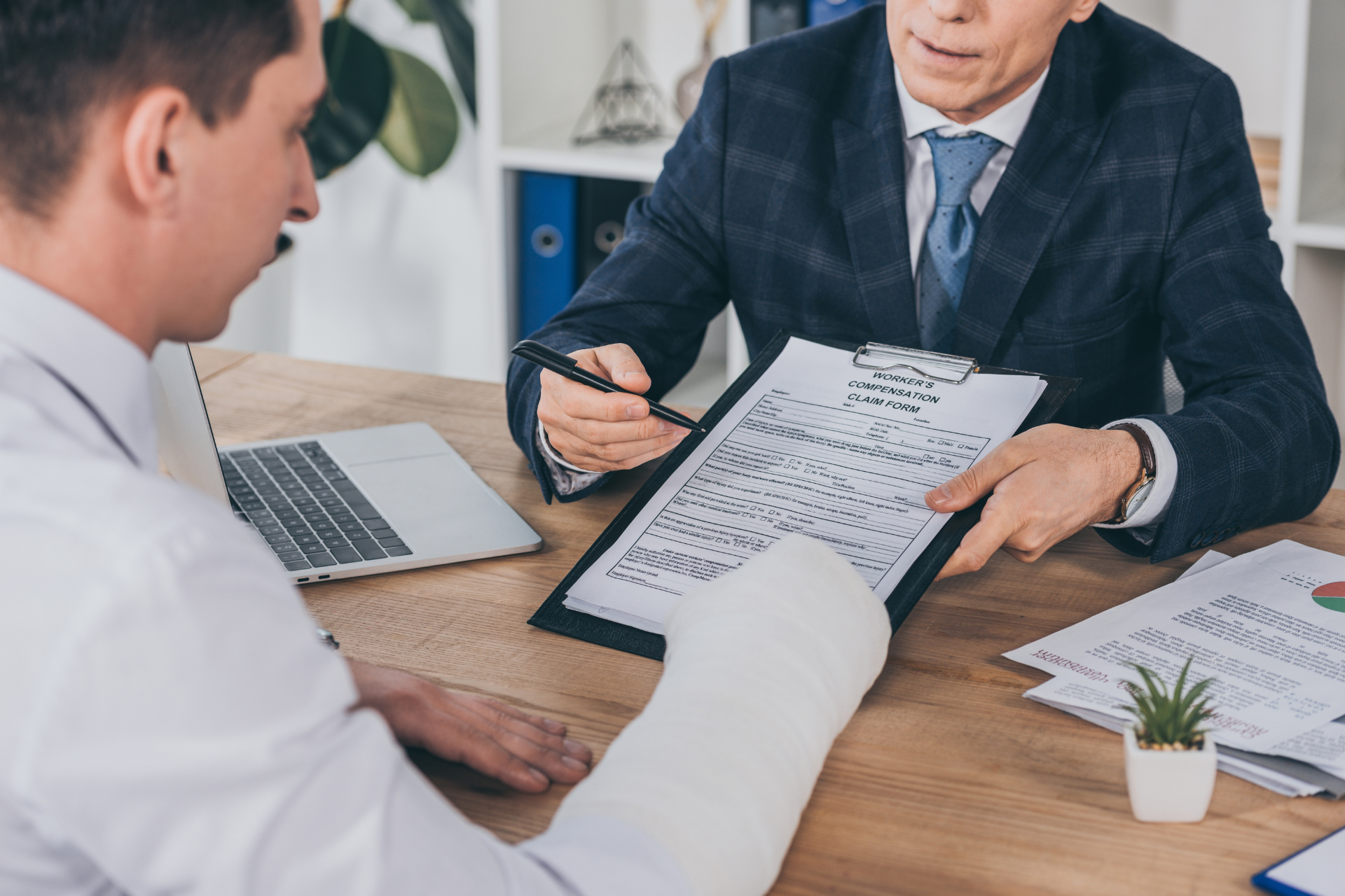 A man with a cast on his leg is sitting at a table talking to a doctor.