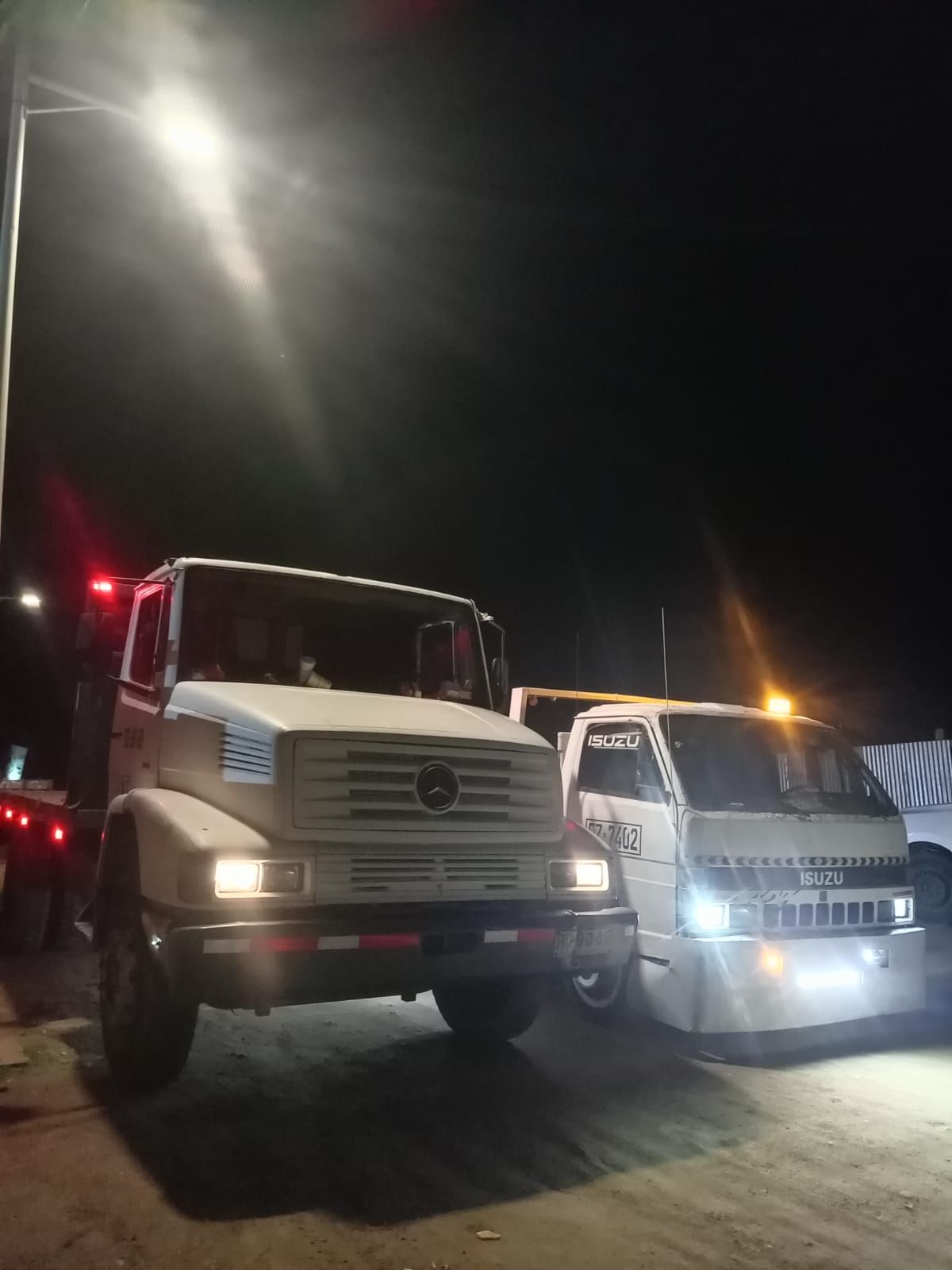 Dos camiones blancos están estacionados uno al lado del otro en un estacionamiento por la noche.