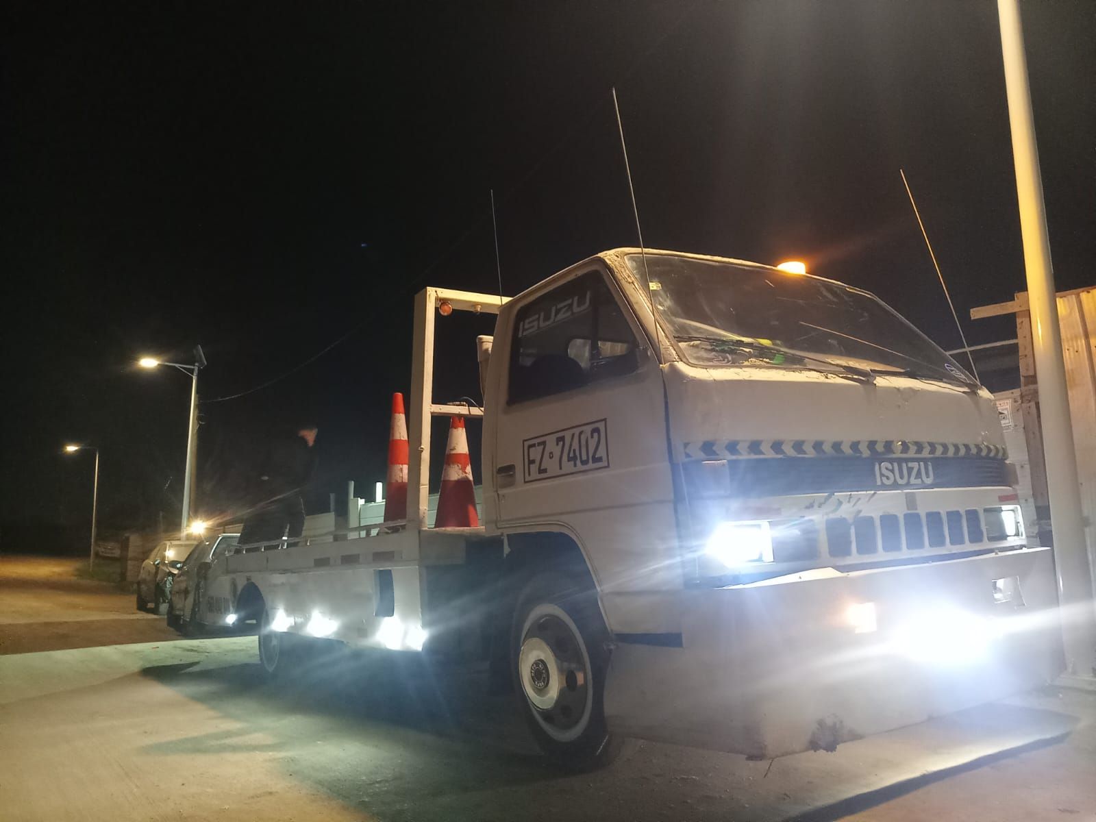 Una grúa Isuzu blanca está estacionada al costado de la carretera por la noche.