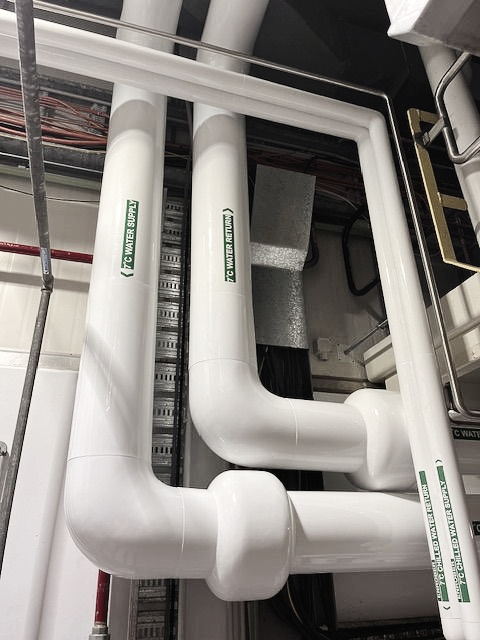 White PVC insulated pipes, bends, mounted in a utility room.