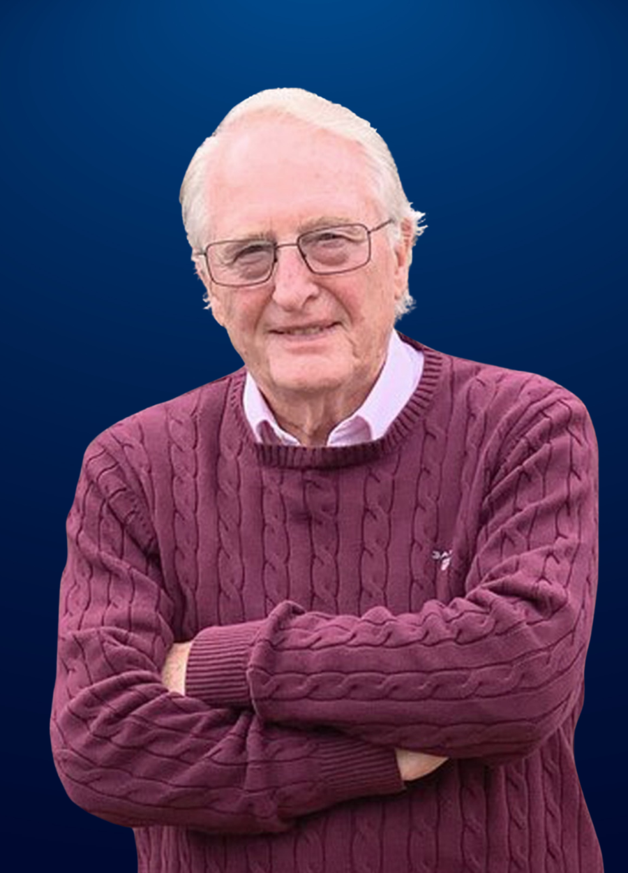 An man wearing a purple sweater and glasses is standing with his arms crossed.