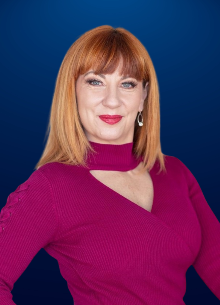 A woman with red hair is wearing a purple sweater and earrings.