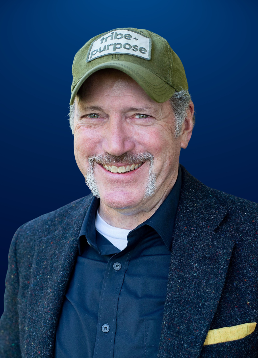 A man wearing a hat and a suit is smiling for the camera.