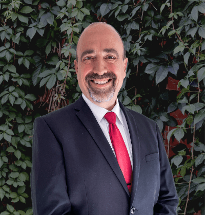 A man in a suit and tie is smiling in front of a bush.