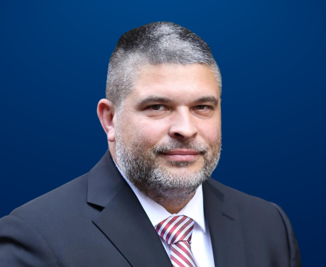 A man in a suit and tie is standing in front of a blue background.