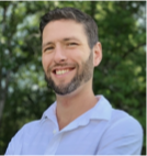 A man with a beard is smiling for the camera while wearing a white shirt.