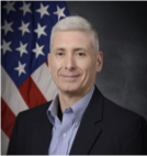 A man in a suit is standing in front of an american flag.