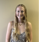 A woman with long blonde hair is smiling for the camera while standing in front of a wall.