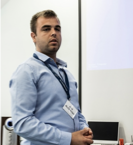 A man in a blue shirt is standing in front of a white board.