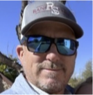 A man wearing sunglasses and a baseball cap is smiling for the camera.