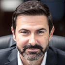 A man with a beard and a suit is sitting in a chair.