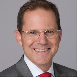 A man wearing glasses and a suit is smiling for the camera.