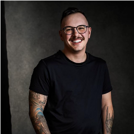 A man with glasses and a mustache is wearing a black shirt and smiling.