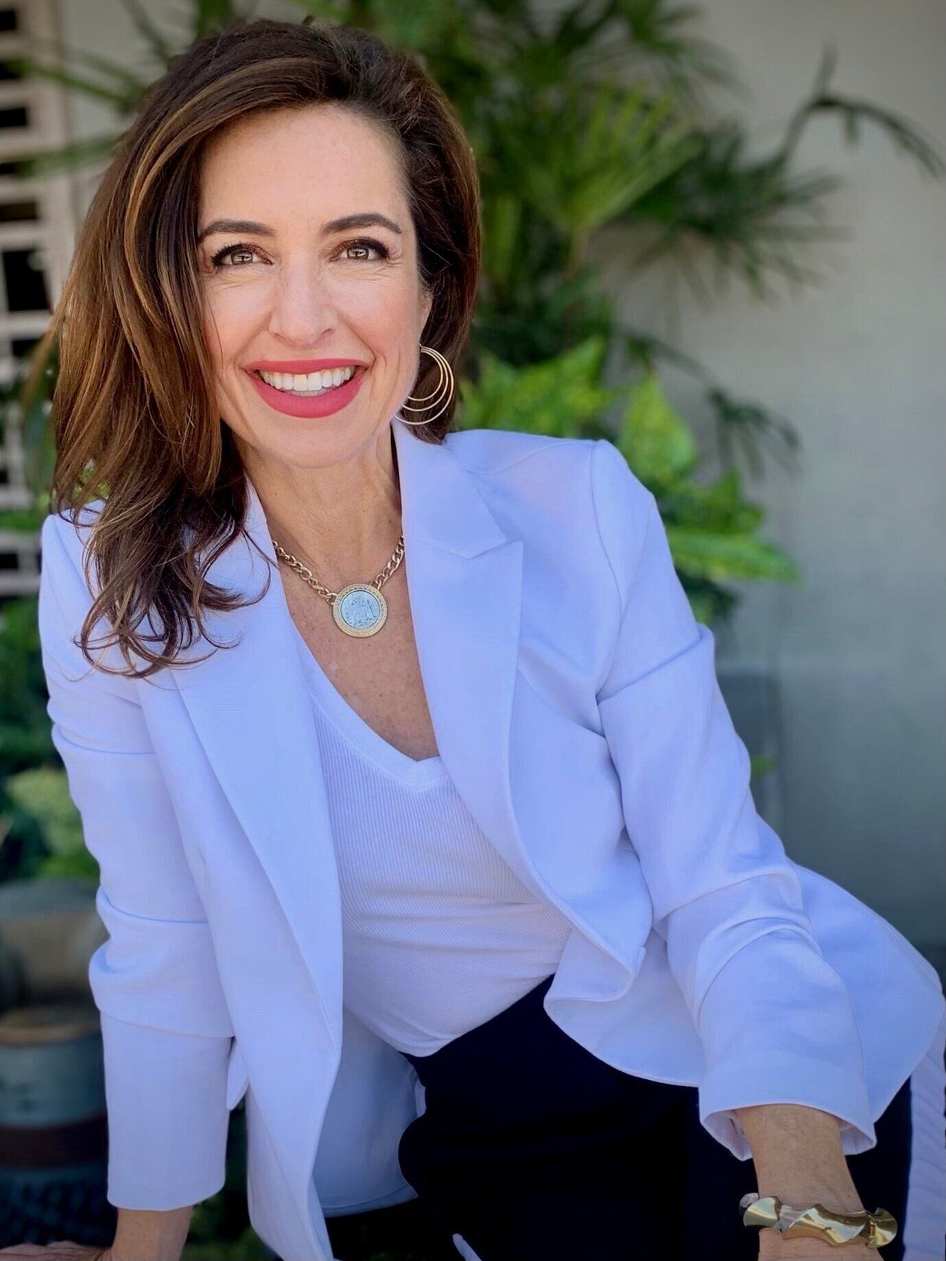 A woman wearing a white jacket and a necklace is smiling for the camera.