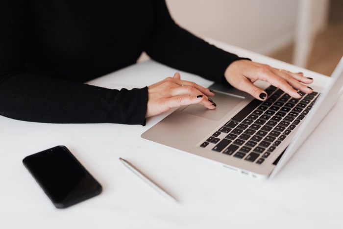 Hands typing on a laptop beside a smartphone and pen on a white desk