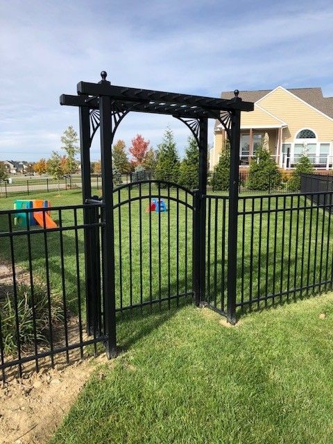 A black fence with a gate leading to a yard with a house in the background