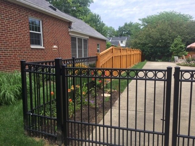 A black fence surrounds a driveway and a brick house.