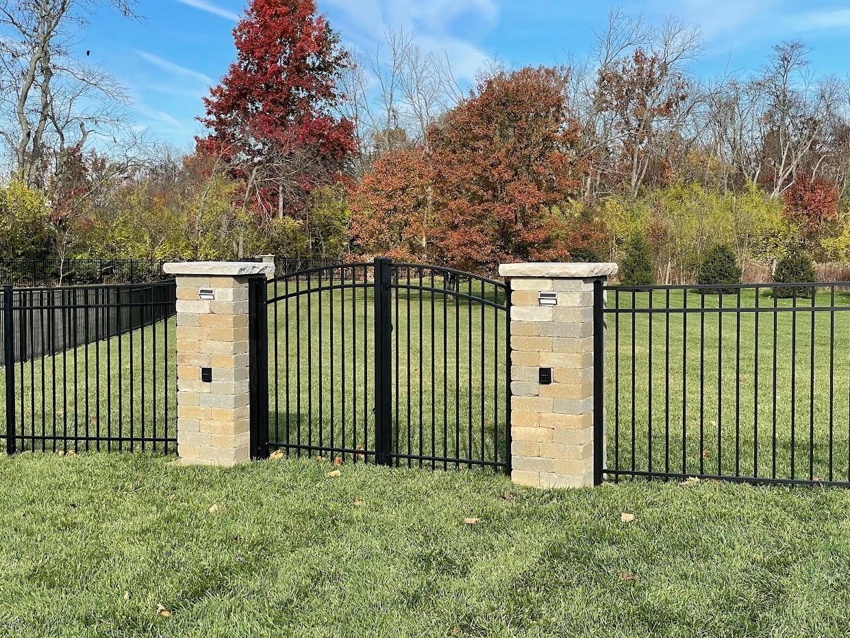 A metal fence with two stone pillars in the middle of a lush green field.