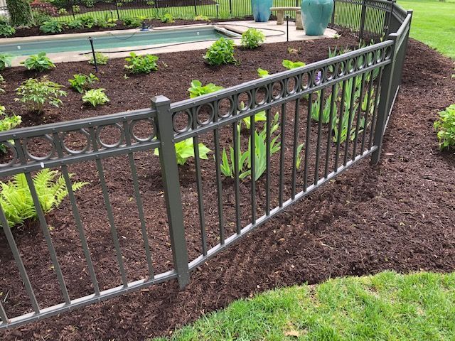 A metal fence surrounds a garden with a pool in the background.