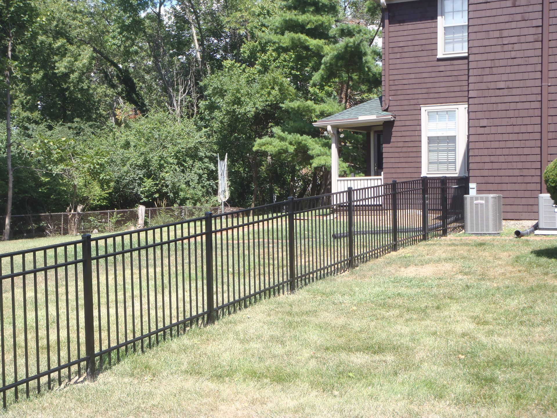 A long black metal fence surrounds a grassy area.