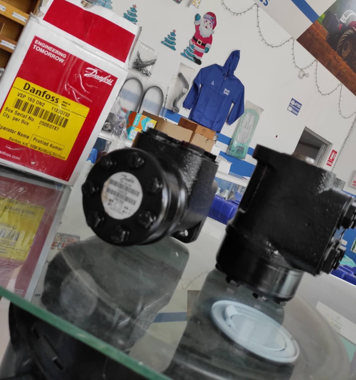 Dos unidades de dirección hidráulica negras sobre una superficie de vidrio, con la caja de Danfoss visible.