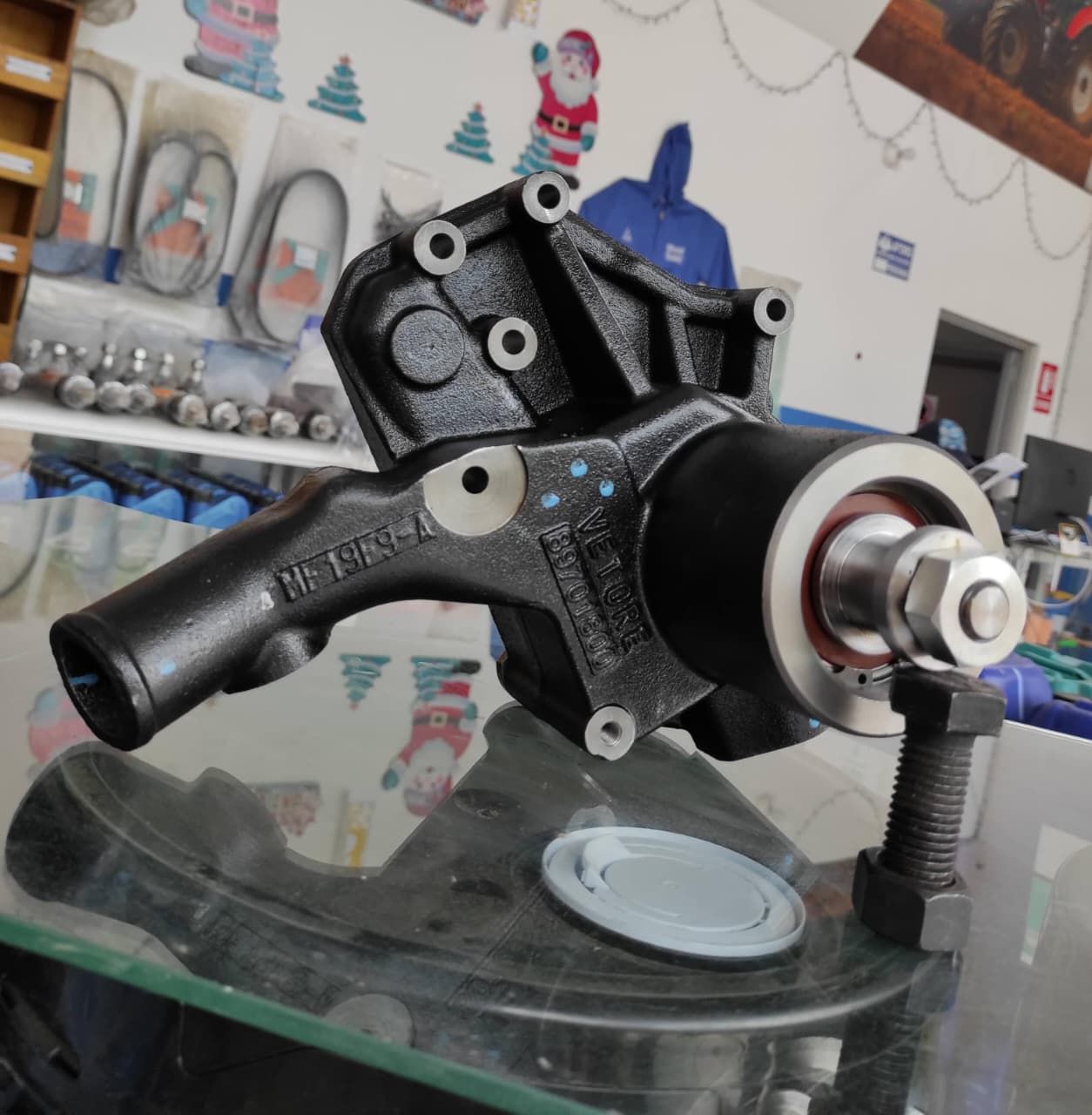 Bomba de agua de metal negro con tuerca y perno sobre superficie de vidrio.