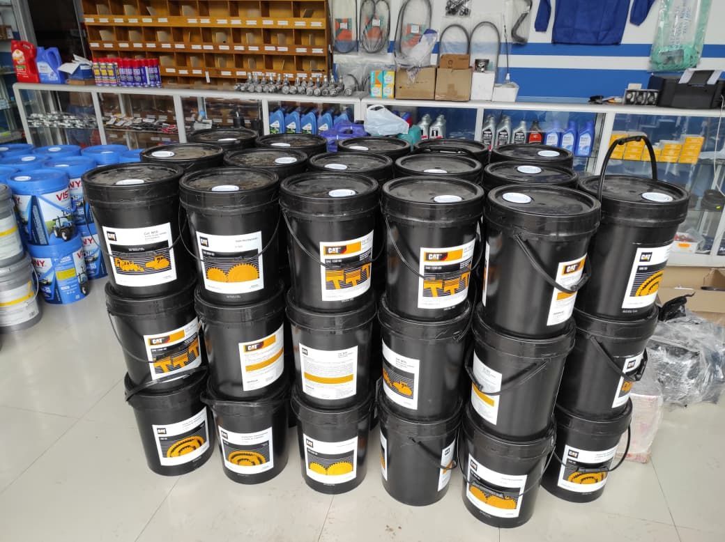 Cubos negros de líquido automotriz apilados dentro de una tienda con estantes y suministros en el fondo.