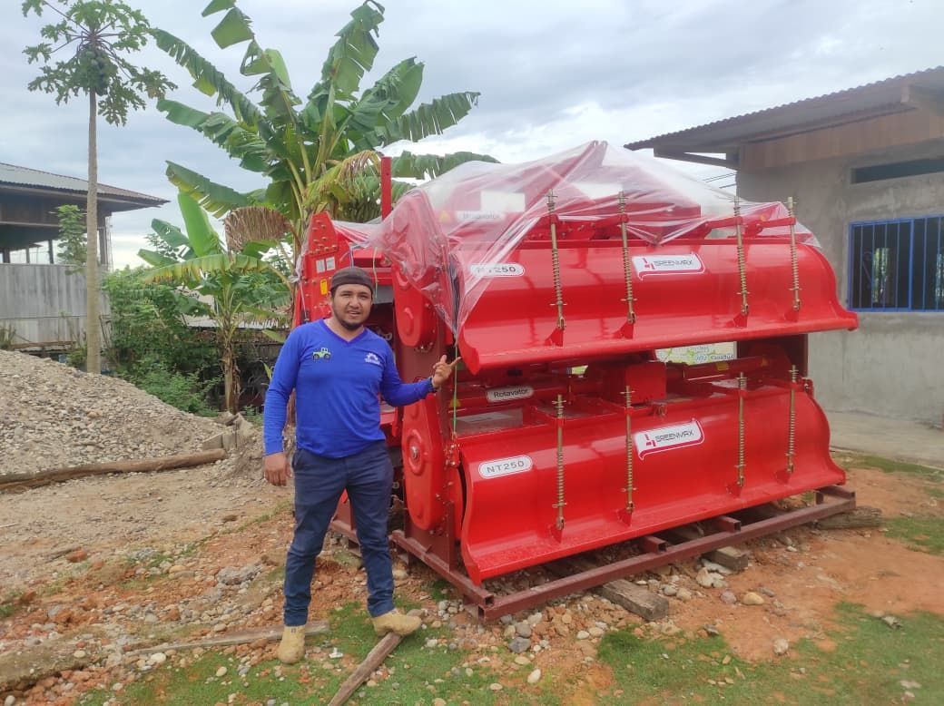 Hombre junto a una maquinaria agrícola roja nueva. Afuera, día nublado.