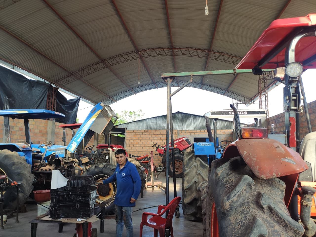 Un hombre con uniforme azul se encuentra en un taller de reparación con tractores.