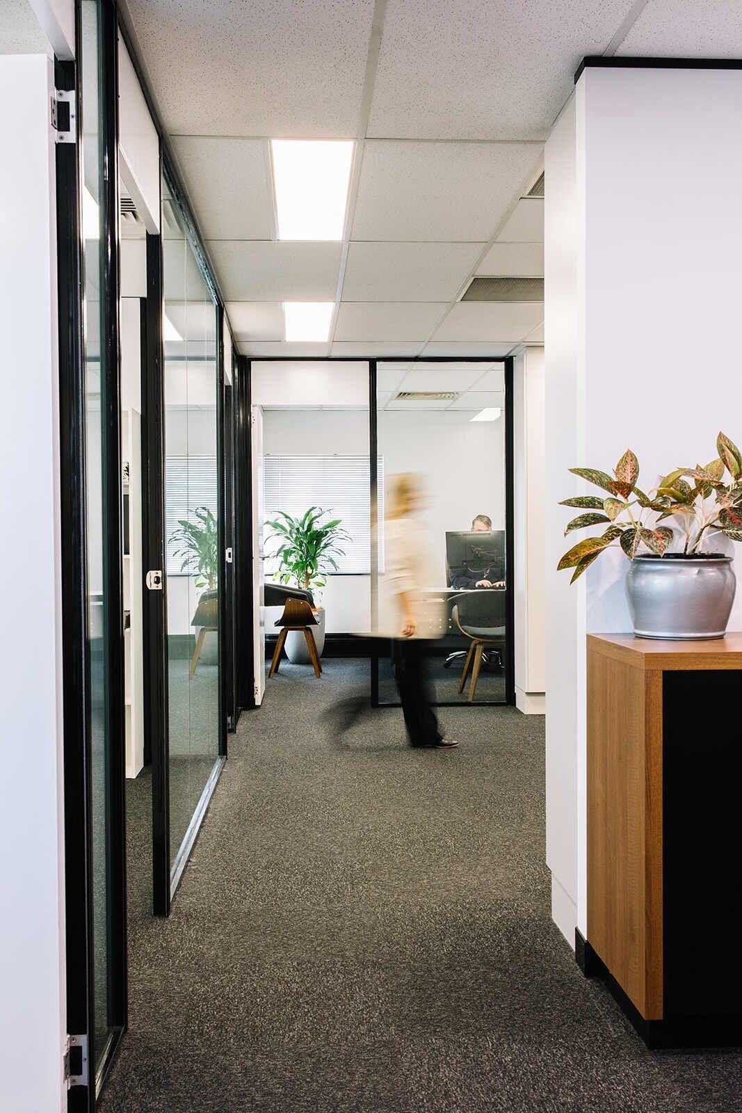 A Woman Is Walking Down A Hallway In An Office Building — The Garis Group  In Hamilton, NSW