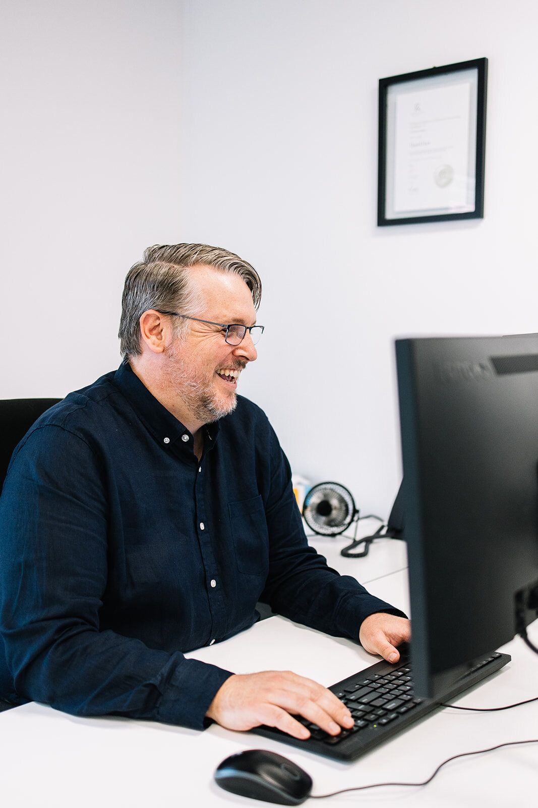 A Man Is Sitting At A Desk In Front Of A Computer — The Garis Group In Hamilton, NSW