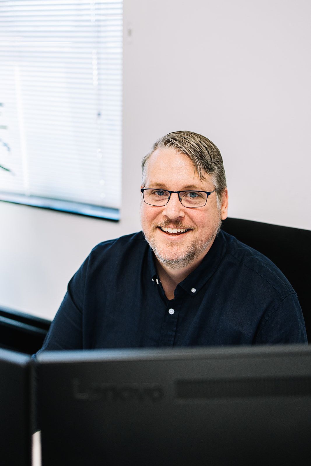 A Man With Glasses Is Sitting In Front Of A Computer Monitor — The Garis Group In Hamilton, NSW