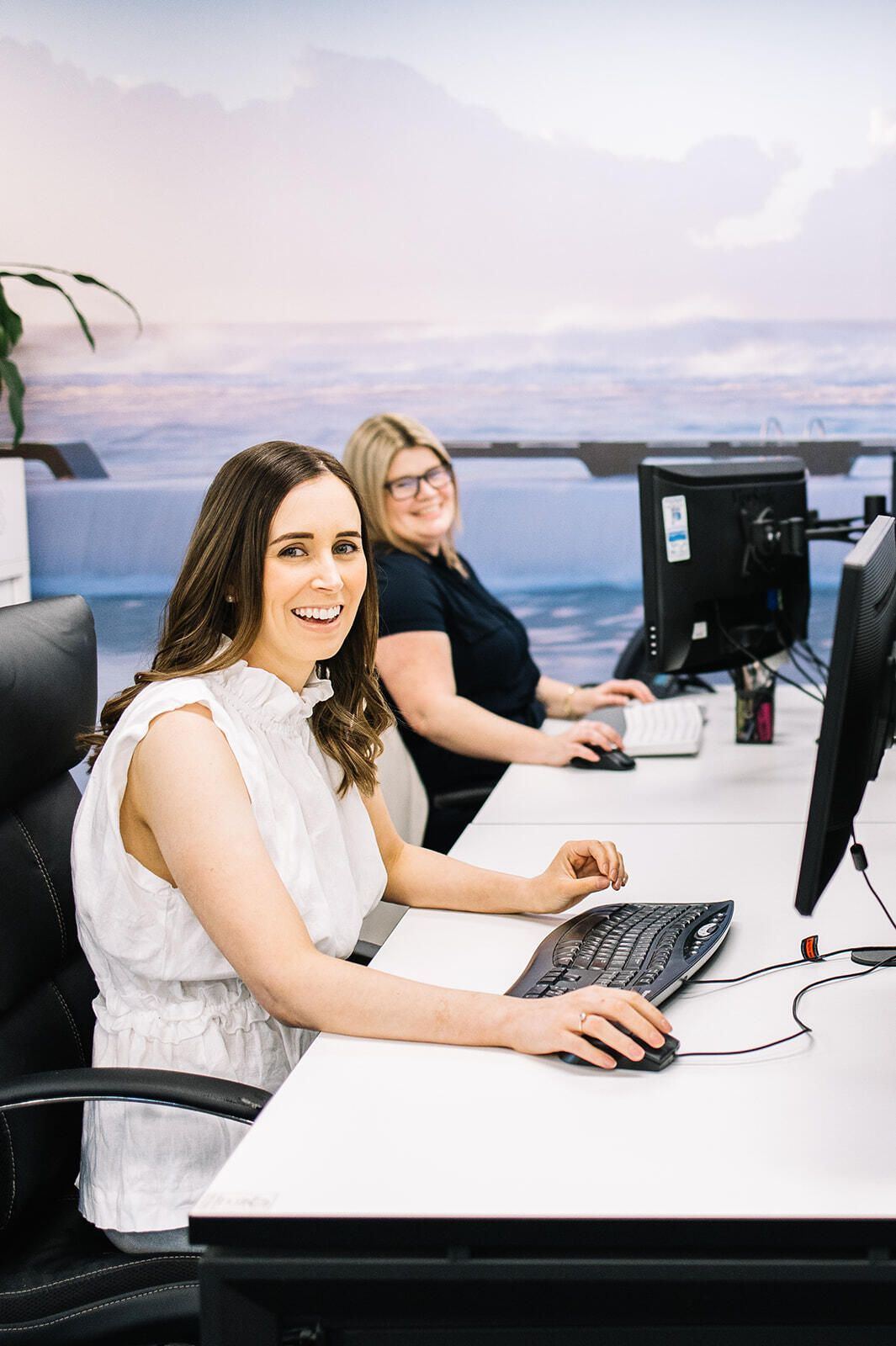 Two Women Are Sitting At Desks In Front Of Computer Monitors — The Garis Group In Sydney, NSW