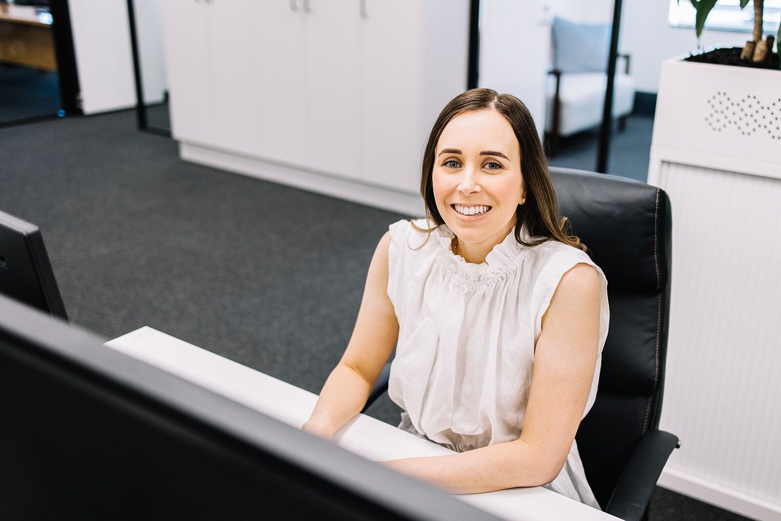 A Woman Is Sitting At A Desk In Front Of A Computer And Smiling — The Garis Group In Hamilton, NSW
